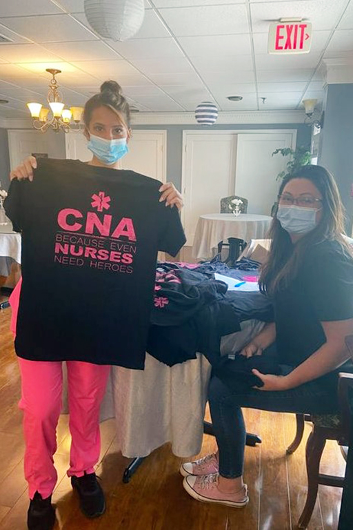 Evergreen House CNA Monica Garcia holding up the T-shirt, with Tara Panciotti, director of nursing, seated