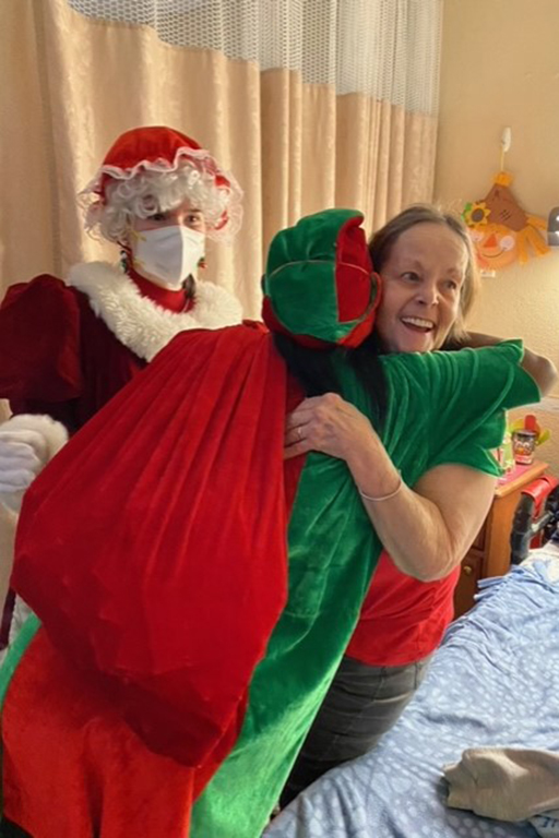 Rivergate Health Care Center resident Christie Madrigal hugging elf Toni Donald, activity assistant, while Mrs. Claus (Audrey Scibilia, activity assistant) looks on