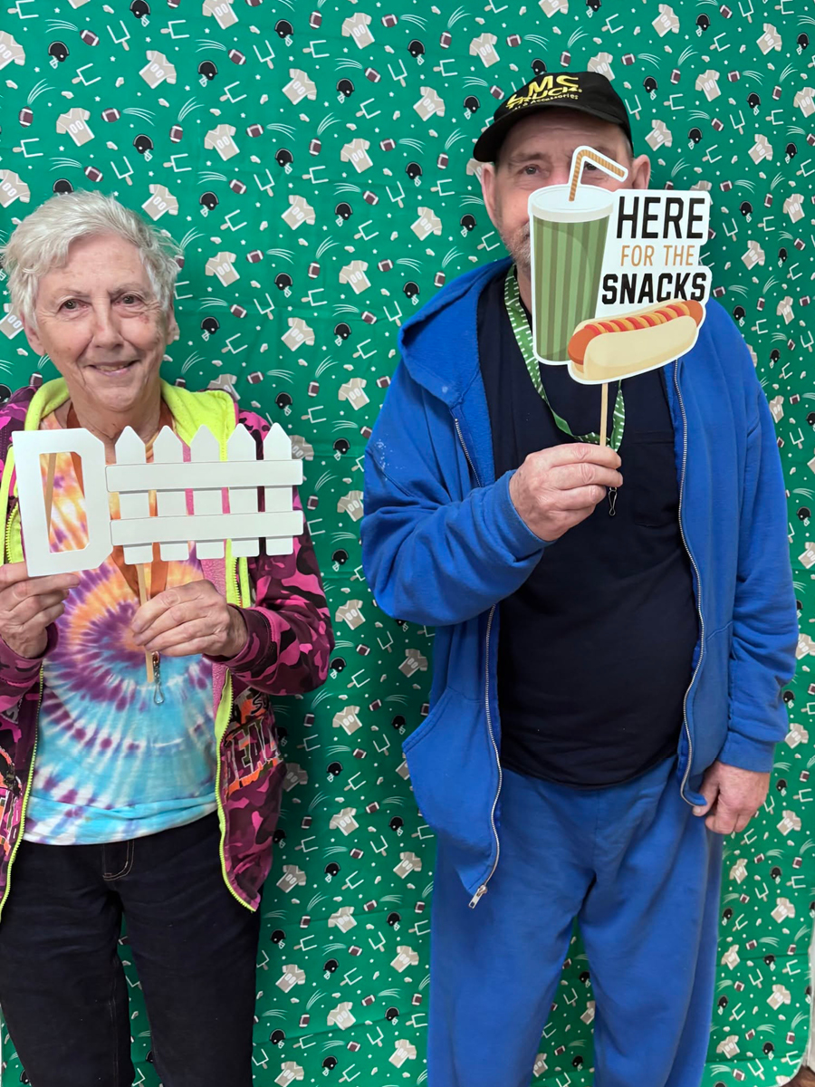 Football.jpg Two seniors smiling in front of a football-themed backdrop, holding fun hand signs